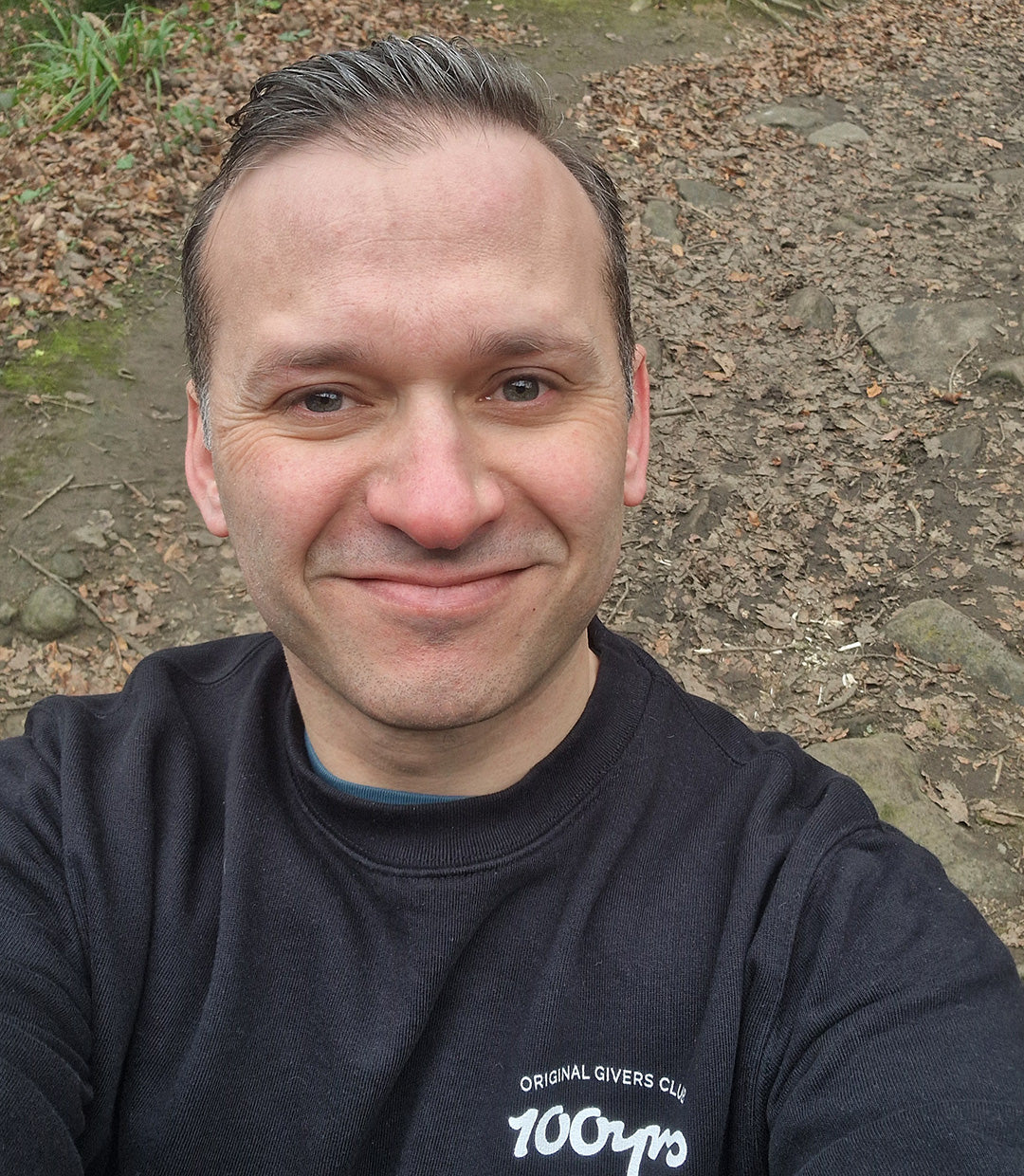 A smiling man wearing a black 100yrs organic cotton sweatshirt.