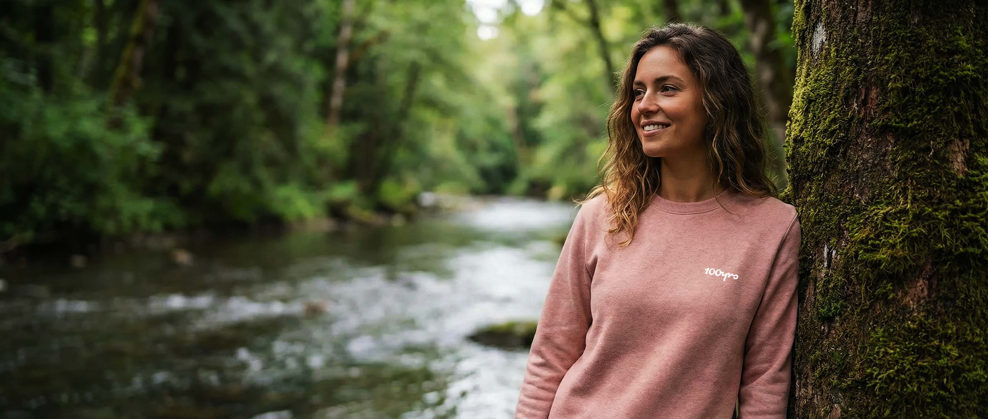 Woman in a pink sweatshirt standing by a stream in a forest
